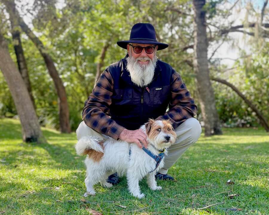 A smiling bearded man wearing a hat with his small dog in Macintosh Island park